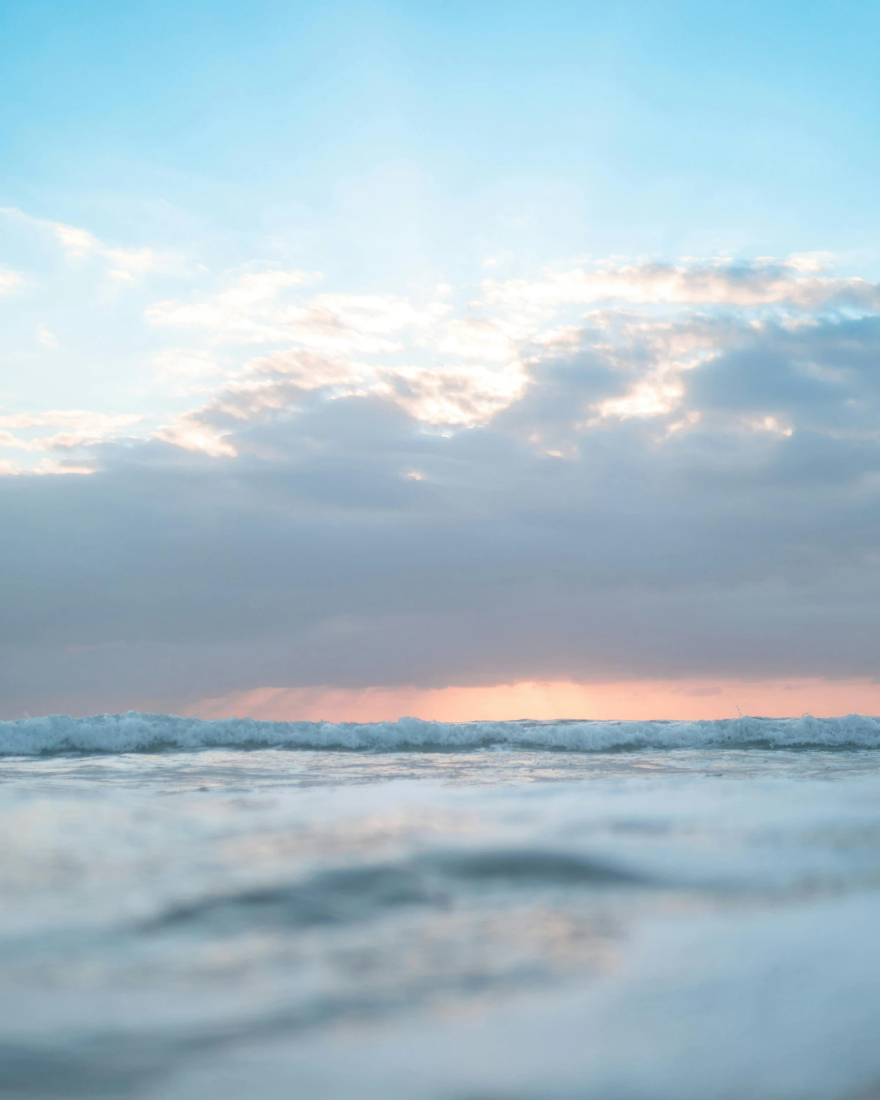 a man riding a surfboard on top of a wave, a picture, unsplash contest winner, minimalism, sunset with cloudy skies, the sky is pink, 3 layers of sky above each other, photo of the middle of the ocean