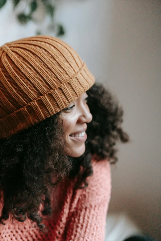 a woman sitting on a couch wearing a knit hat, trending on pexels, dark short curly hair smiling, warm color clothes, sza, zoomed in