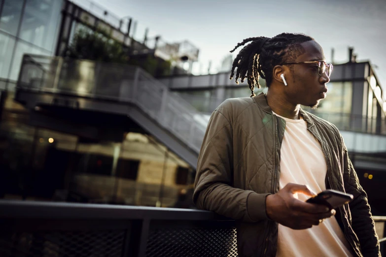 a man with dreadlocks looking at his cell phone, trending on pexels, on rooftop, earbuds jewelry, back lit, portrait of tall