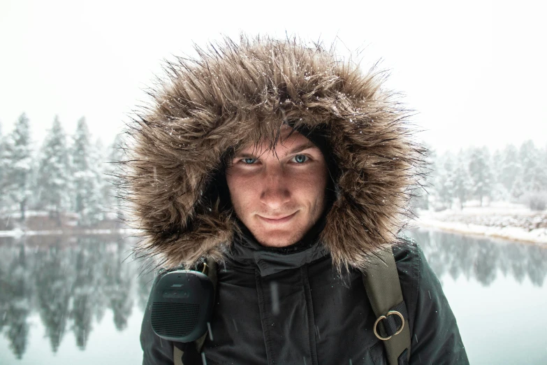 a man standing in front of a lake in the snow, a picture, avatar image, fur hood, close up portrait photo, jakub gazmercik
