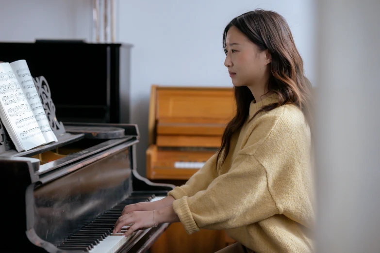 a woman in a yellow sweater playing a piano, inspired by Song Xu, pexels contest winner, mingei, in a medium full shot, still frame from a movie, casually dressed, high delicate details