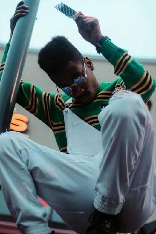 a man sitting on top of a metal pole, an album cover, trending on unsplash, happening, wearing a green sweater, wearing white suit and glasses, black teenage boy, ( ( theatrical ) )