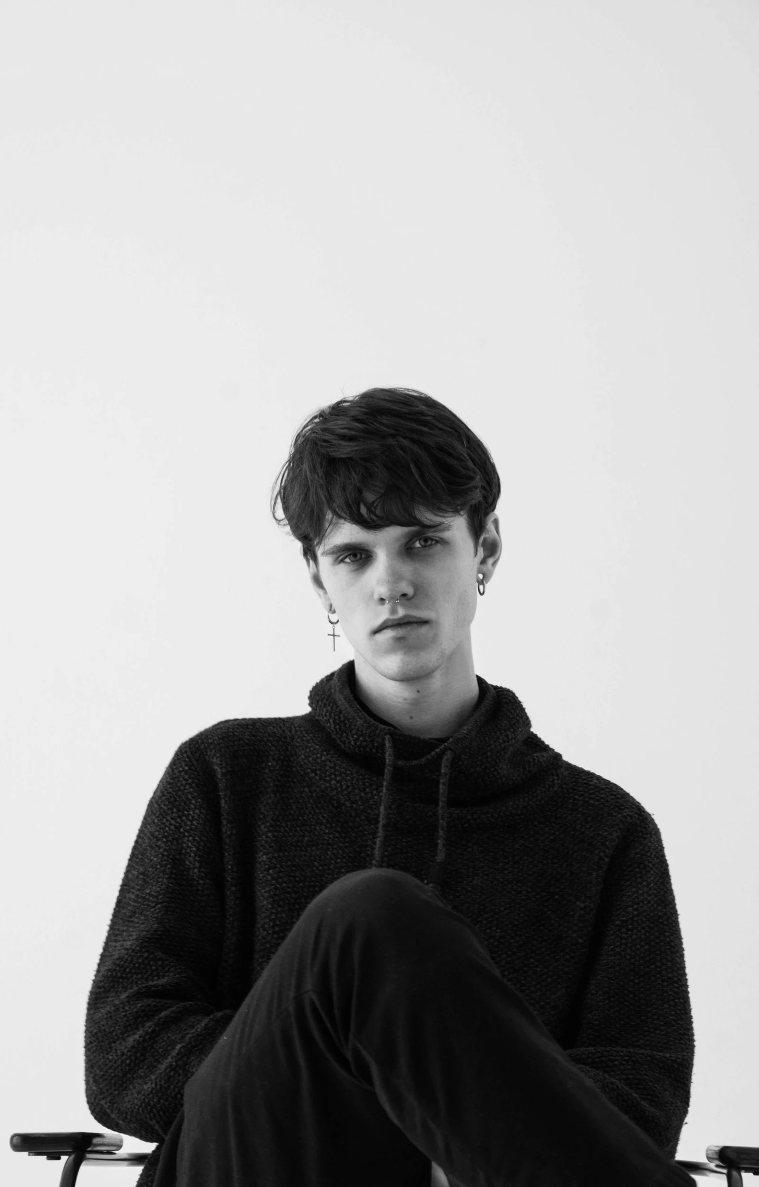 a black and white photo of a man sitting in a chair, an album cover, unsplash, bauhaus, declan mckenna, wearing a black sweater, frown fashion model, portrait of young man