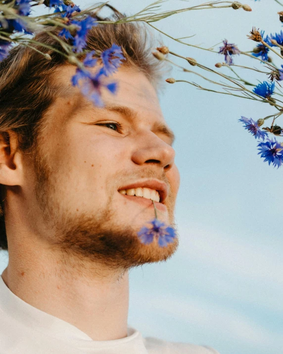 a man with a flower crown on his head, trending on unsplash, romanticism, blue flowers accents, lgbtq, smileing nright, with pale skin