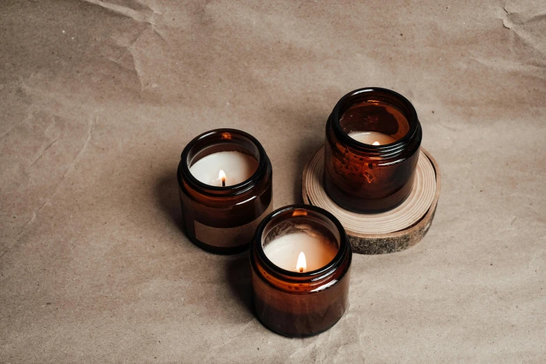 three brown glass candles sitting on top of a piece of wood, unsplash, minimalism, glass jar, skincare, multiple stories, various items