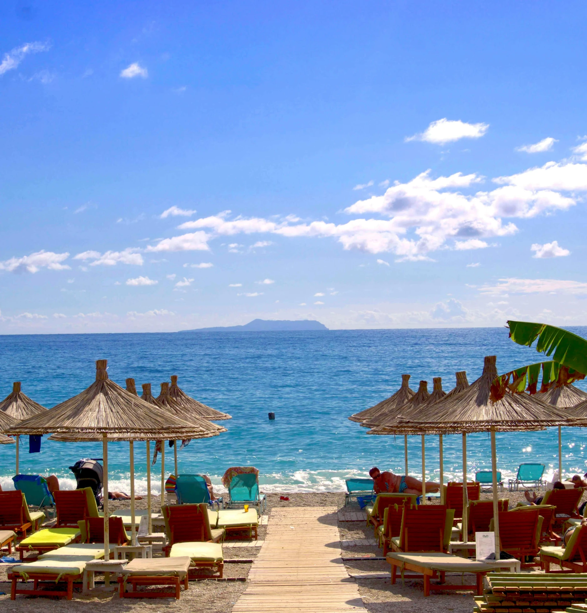 a beach filled with lots of umbrellas next to the ocean, marbella, bamboo huts, greek setting, sky blue