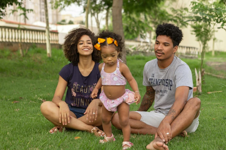 a couple of people that are sitting in the grass, a portrait, by Lily Delissa Joseph, pexels contest winner, portrait of family of three, tan skin a tee shirt and shorts, brazil, with afro