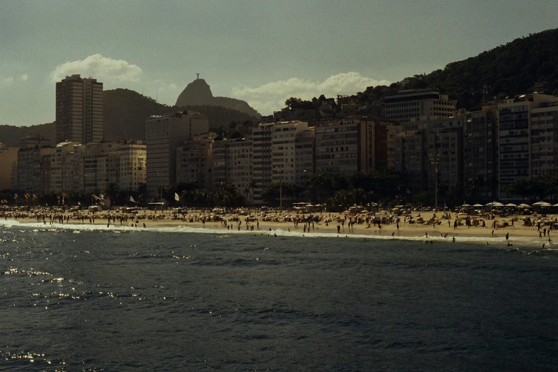 a group of people standing on top of a beach next to a body of water, a detailed matte painting, by Elsa Bleda, pexels contest winner, hyperrealism, rio de janeiro, 1960's olympics footage, sun and shadow over a city, medium format. soft light