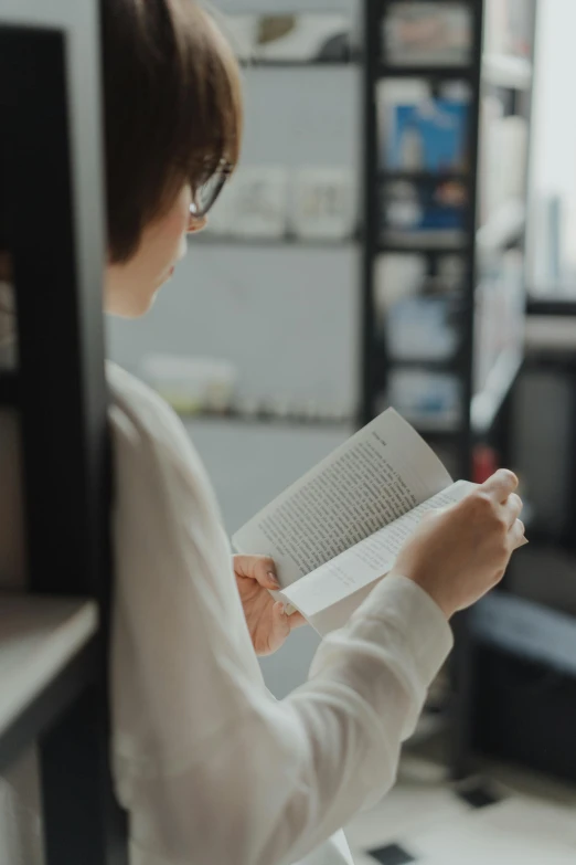 a woman reading a book in a library, pexels contest winner, wearing a white sweater, reading engineering book, gif, casually dressed