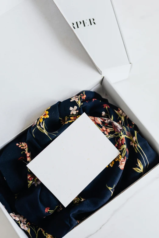 a box that has a scarf in it, inspired by Eden Box, trending on unsplash, hurufiyya, dark blue and white robes, floral details, on white paper, casual clothing