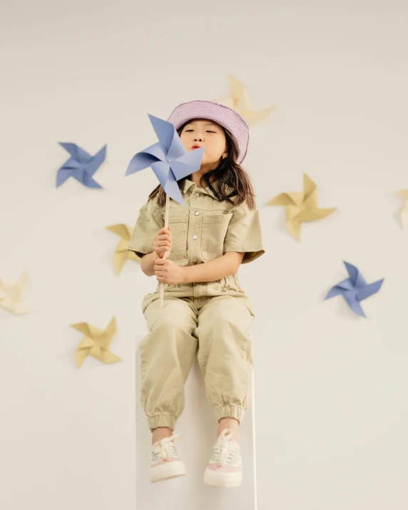 a little girl sitting on top of a box holding a pinwheel, inspired by Weiwei, trending on pexels, wearing human air force jumpsuit, khakis, promotional image, starlight