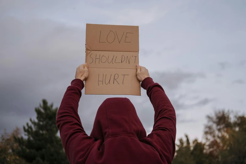a person holding a sign that says love shouldn't hurt, trending on pexels, sots art, shroud, profile image, protest, background image