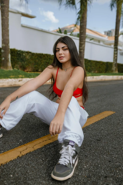 a woman sitting on the side of the road, trending on pexels, red sport clothing, in sao paulo, white pants, madison beer