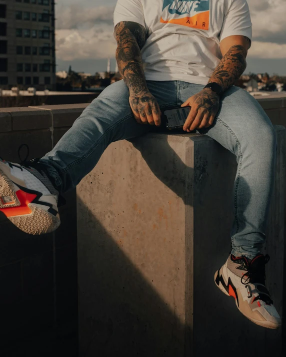 a man sitting on top of a cement block, inspired by Seb McKinnon, trending on pexels, graffiti, jean and multicolor shoes, tattooed skin, lightening, ( ( ( wearing jeans ) ) )