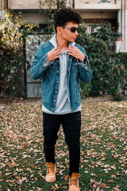 a man standing on top of a lush green field, an album cover, by Robbie Trevino, trending on pexels, realism, wearing a jeans jackets, posing in an urban street, gray hoodie, profile picture