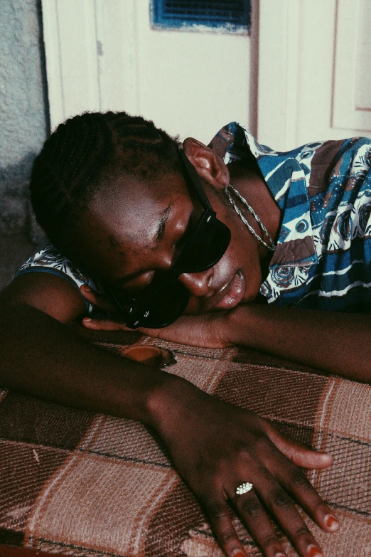 a close up of a person laying on a bed, an album cover, inspired by Ras Akyem, trending on pexels, wearing shades, teenage boy, sittin, african