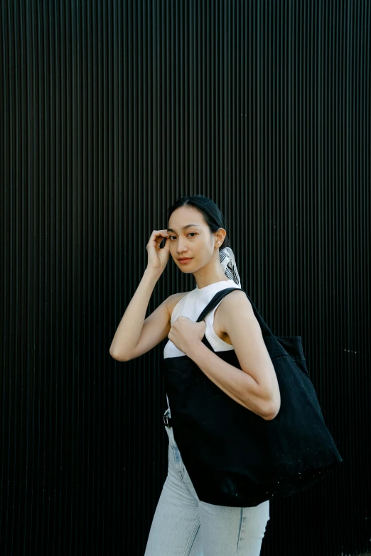 a woman standing in front of a black wall, inspired by Gao Cen, pexels contest winner, minimalism, bag, wearing : tanktop, kiko mizuhara, non-binary