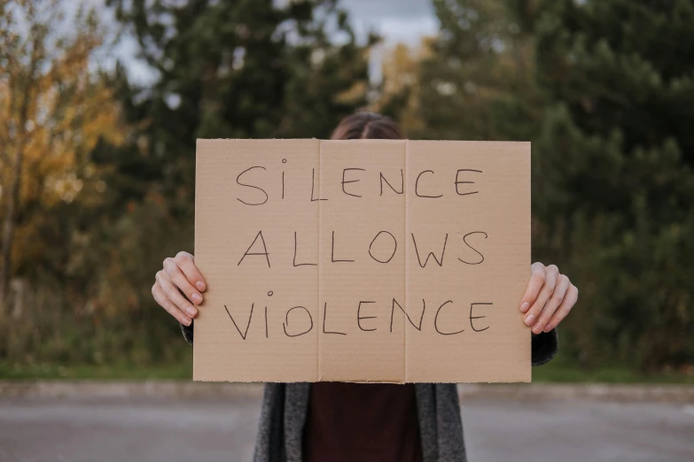 a person holding a sign that says silence allows violence, an album cover, by Emma Andijewska, shutterstock, cardboard, instagram post, bl