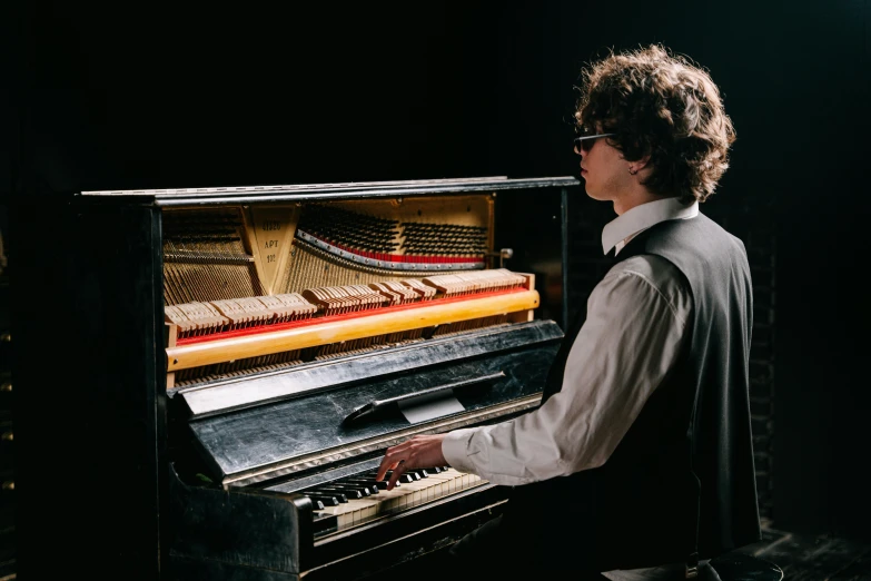 a man playing a piano in a dark room, an album cover, inspired by Michael Ray Charles, unsplash, bauhaus, finn wolfhard, wearing a suit and glasses, high school, ultra realistic classic