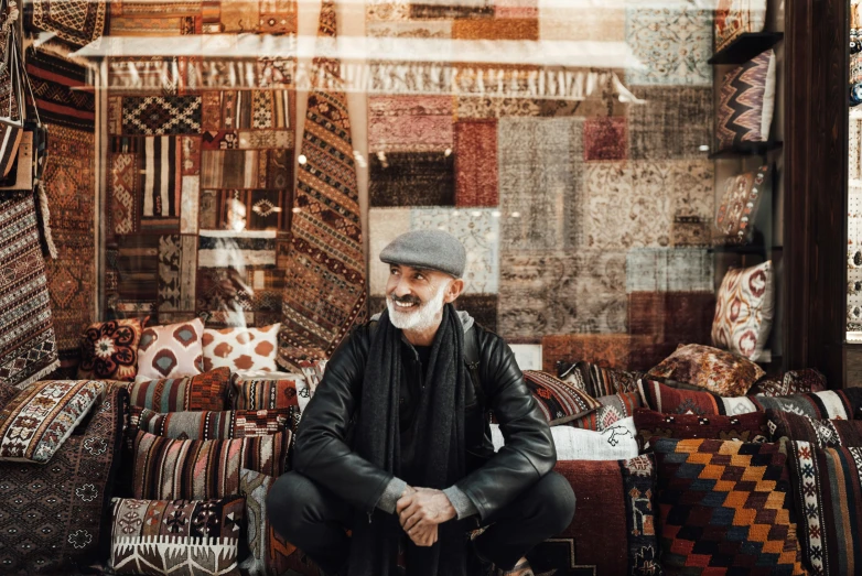 a man sitting on the ground in front of a store, inspired by Edi Rama, unsplash contest winner, hurufiyya, oriental carpets, “portrait of leonard cohen, market stalls, 1 6 x 1 6