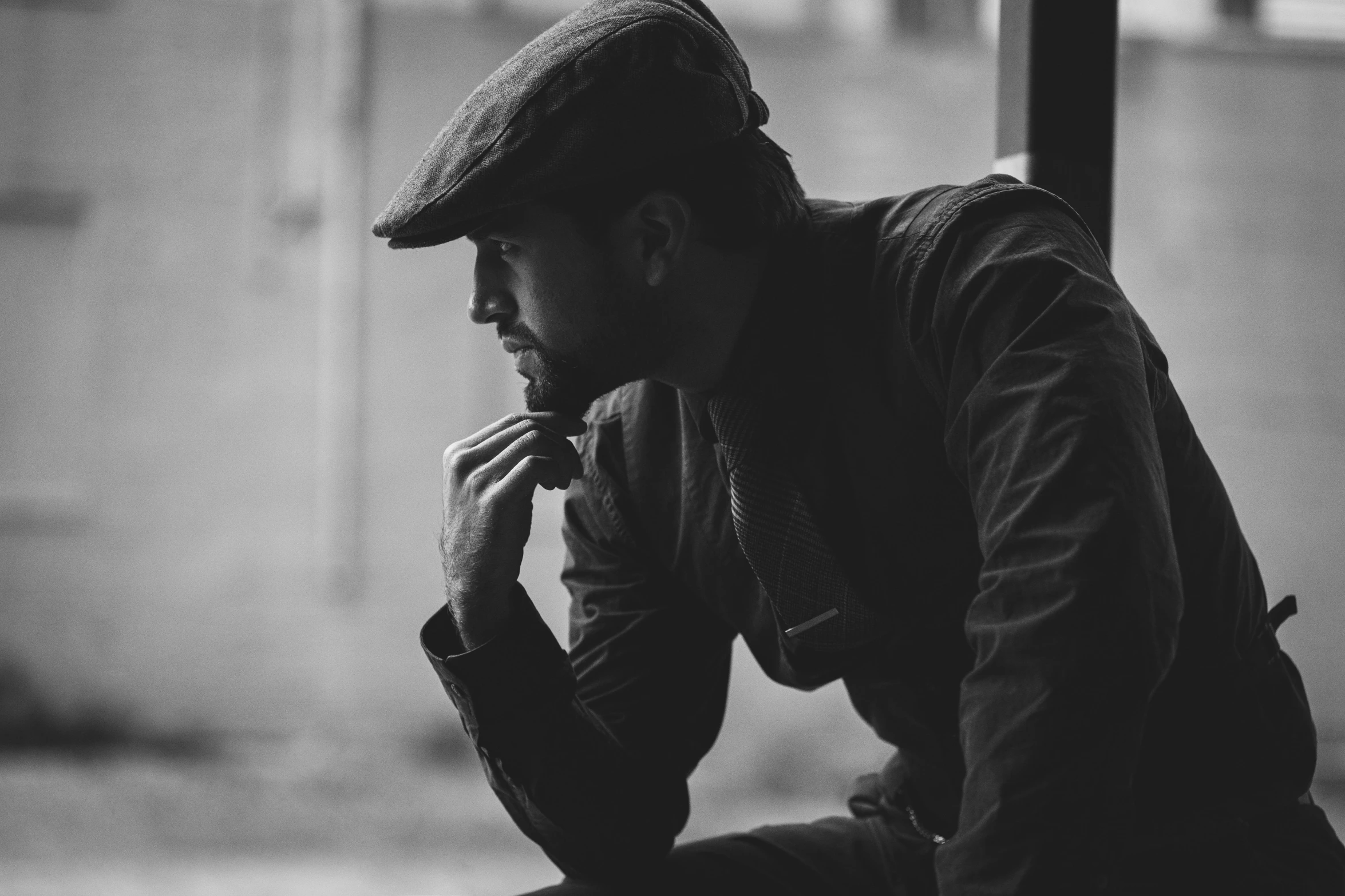 a black and white photo of a man sitting on a bench, unsplash, breton cap, thoughtful pose, leaning against the window, will graham