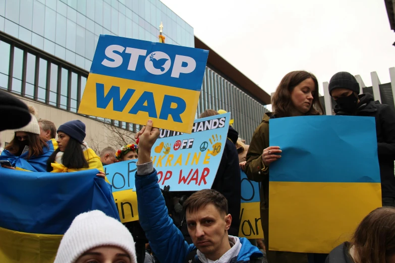 a group of people holding signs in front of a building, war in ukraine, blue and yellow, avatar image, close - up photo