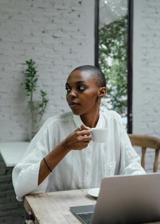 a woman sitting at a table with a laptop and a cup of coffee, pexels contest winner, happening, wearing a white button up shirt, afrocentric mysticism, thoughtful ), low quality photo