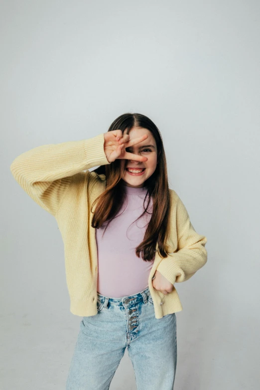 a woman standing in front of a white wall, an album cover, by Grace Polit, trending on pexels, wearing a yellow hoodie, pose(arms up + happy), violet myers, teenager girl