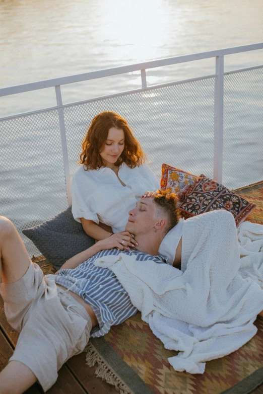 a man and a woman laying on a bed next to a body of water