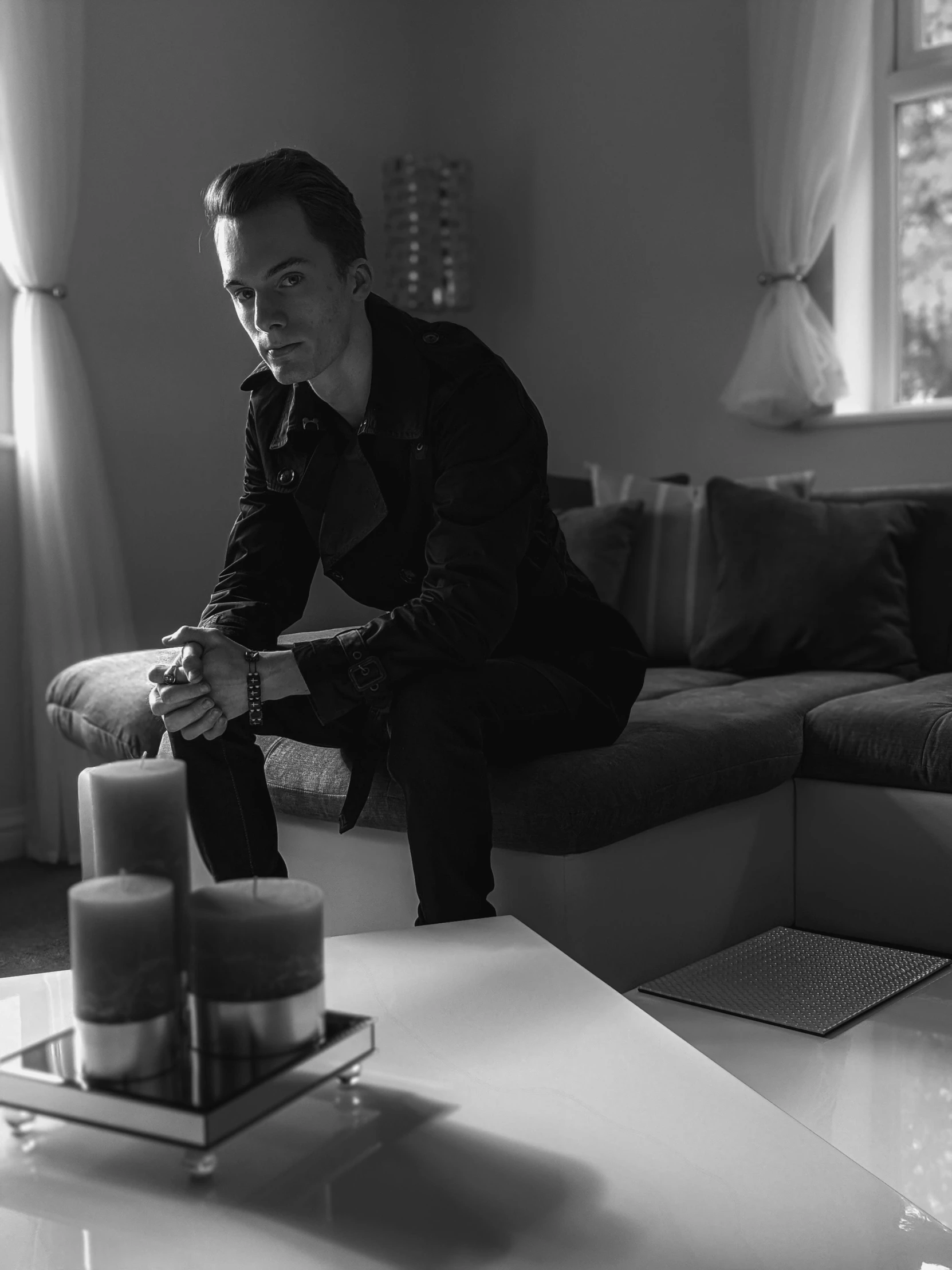 a man sitting on a couch in a living room, a black and white photo, by Emma Andijewska, frank dillane, room full of candles, profile image, julian ope
