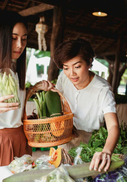 a couple of women standing next to each other at a table, pexels contest winner, confident holding vegetables, avatar image, market setting, asian female