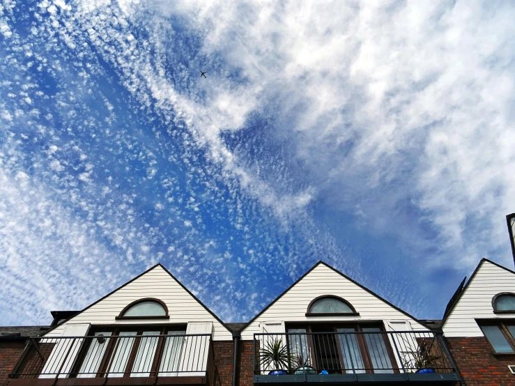 a couple of windows sitting on the side of a building, by Carey Morris, unsplash, precisionism, cirrus clouds, cottages, wide angel shot from below, balconies