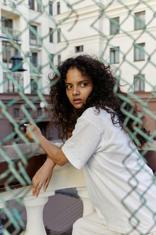 a woman leaning against a fence holding a tennis racquet, an album cover, pexels contest winner, renaissance, tessa thompson, young middle eastern woman, wearing white clothes, behind bars