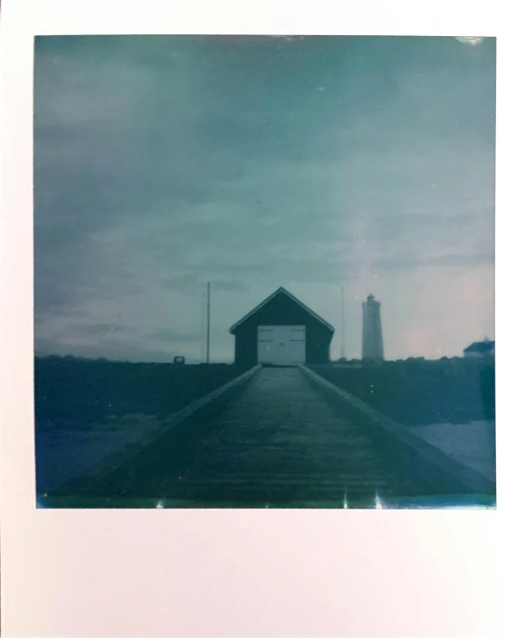 a picture of a dock with a lighthouse in the background, a polaroid photo, solarised, pictured from the shoulders up, muted coloures, low quality print