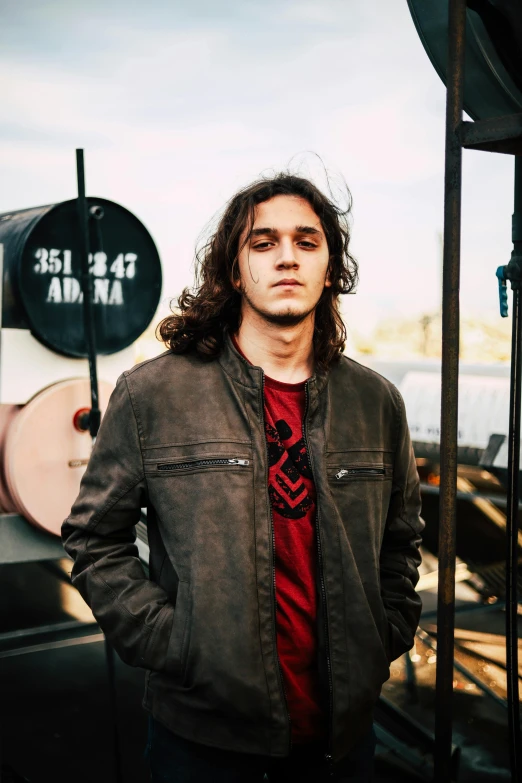 a man standing in front of a train, inspired by Jeremy Henderson, pexels contest winner, antipodeans, long hair and red shirt, robert sheehan, profile image, wearing jeans and a black hoodie