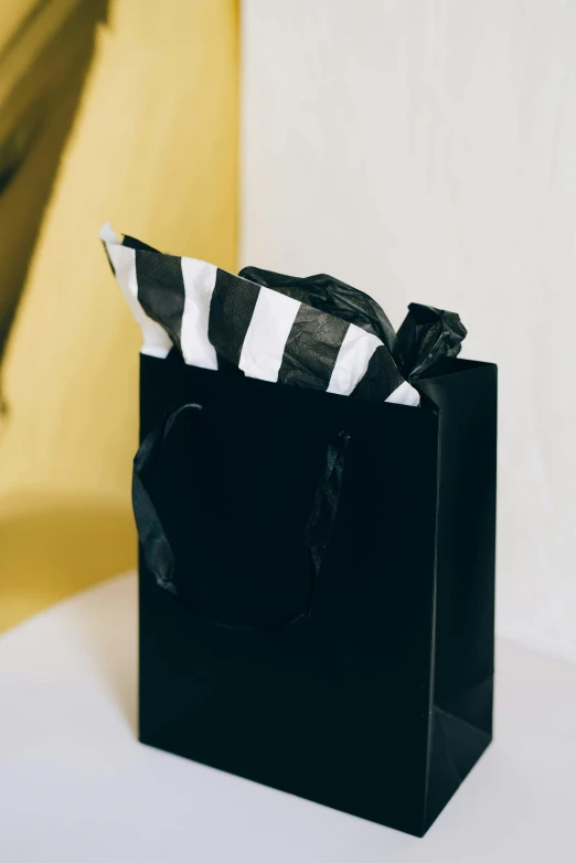 a black bag sitting on top of a white table, holding gift, on a yellow paper, black stripes, dark. no text