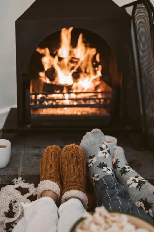 a person sitting in front of a fireplace with a cup of coffee, slippers, manuka, al fresco, mittens