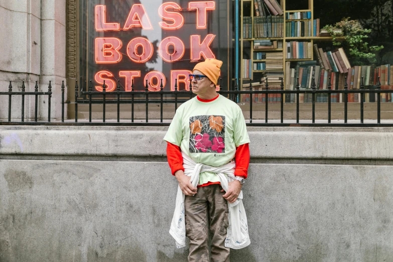 a man leaning against a wall in front of a book store, by Julia Pishtar, visual art, graphic tees, wearing a red backwards cap, dayglo, the last portrait of mac miller