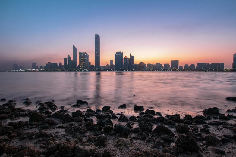 a large body of water with a city in the background, by Daniel Lieske, pexels contest winner, hurufiyya, on the beach during sunset, ameera al-taweel, skyline showing, youtube thumbnail