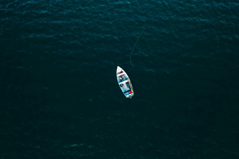 a small boat floating on top of a body of water, by Elsa Bleda, pexels contest winner, fishing pole, deep blue oceans, aerial, dark dingy