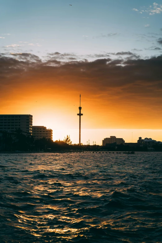 the sun is setting over a body of water, by Sebastian Spreng, pexels contest winner, auckland sky tower, palast der republik in berlin, golden hues, viewed from the ocean