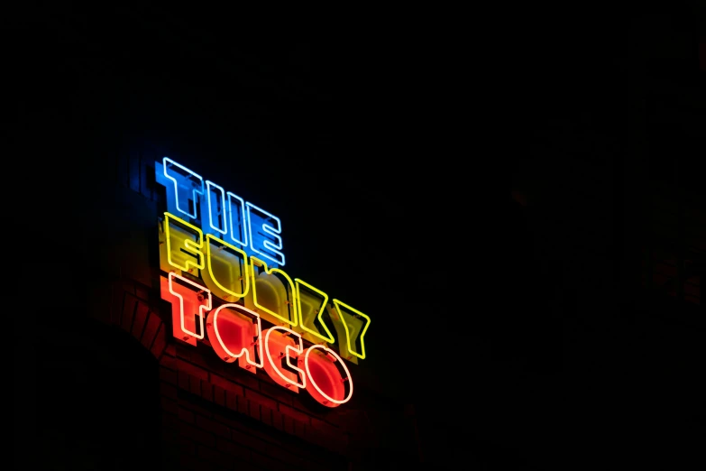 a neon sign on the side of a building, taco, fuzzy, with a black background, thumbnail