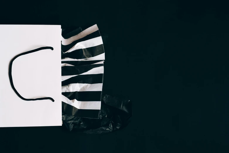 a white paper bag sitting on top of a black table, a black and white photo, unsplash, letterism, left eye stripe, mime, face accessories, torn!! clothing