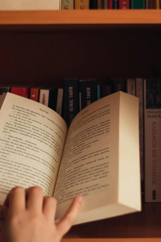 a person reading a book in front of a bookshelf, up close shot, softly - lit, reddit post, half turned around