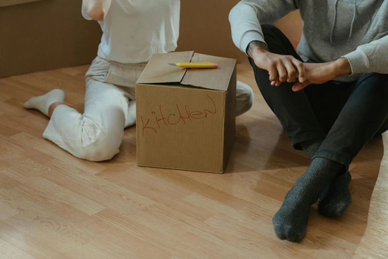 a man and a woman sitting on the floor next to a cardboard box