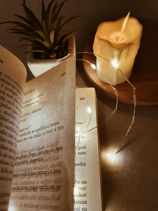 an open book sitting on top of a table next to a lit candle, string lights, instagram story, close up shot from the side, thin glowing wires