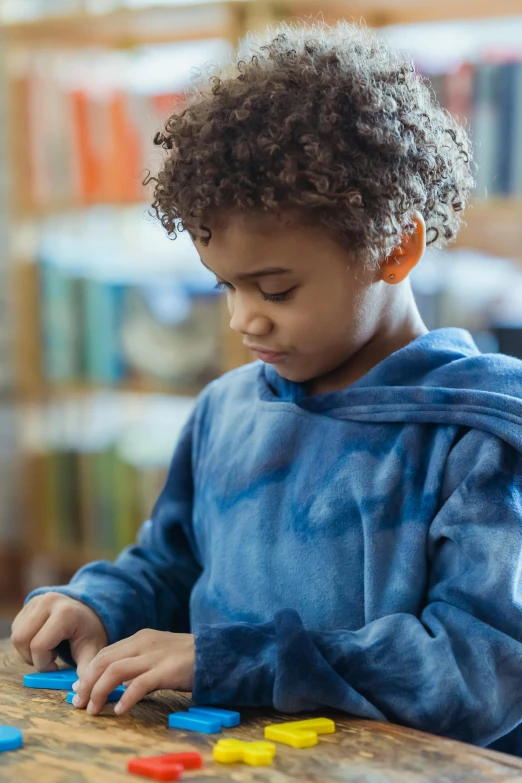 a little boy that is sitting at a table, wearing a blue hoodie, in a library, integrating with technology, thumbnail