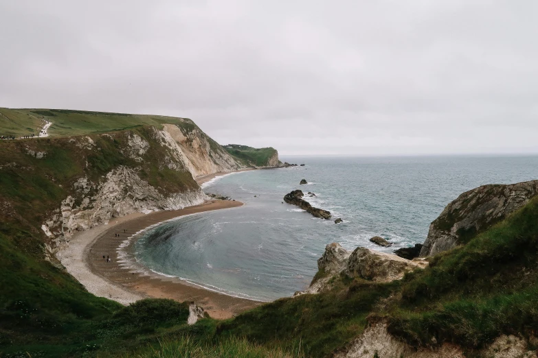 a large body of water sitting on top of a lush green hillside, by Rachel Reckitt, pexels contest winner, chalk cliffs above, victorian arcs of sand, big overcast, john pawson