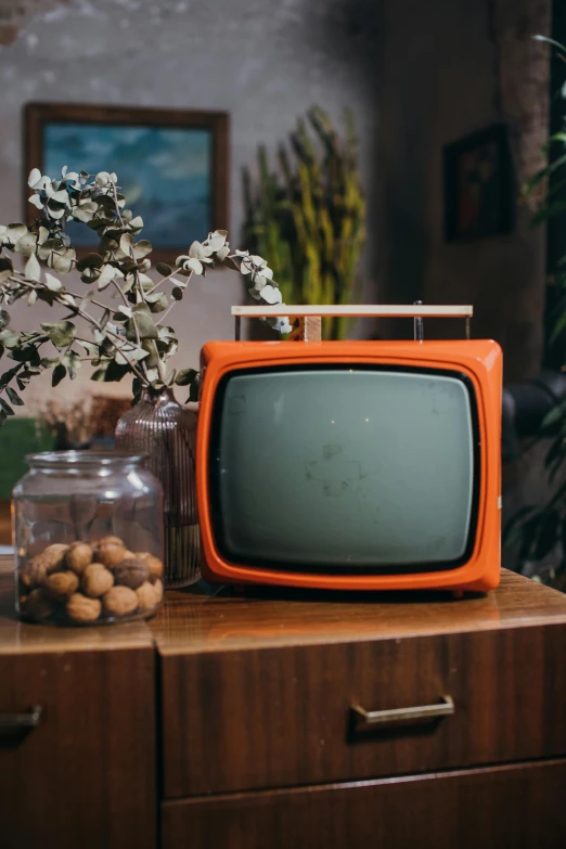 an orange television sitting on top of a wooden table, by Everett Warner, trending on pexels, modernism, vhs cover, tv frame, 1 9 6 0 s, cottagecore hippie