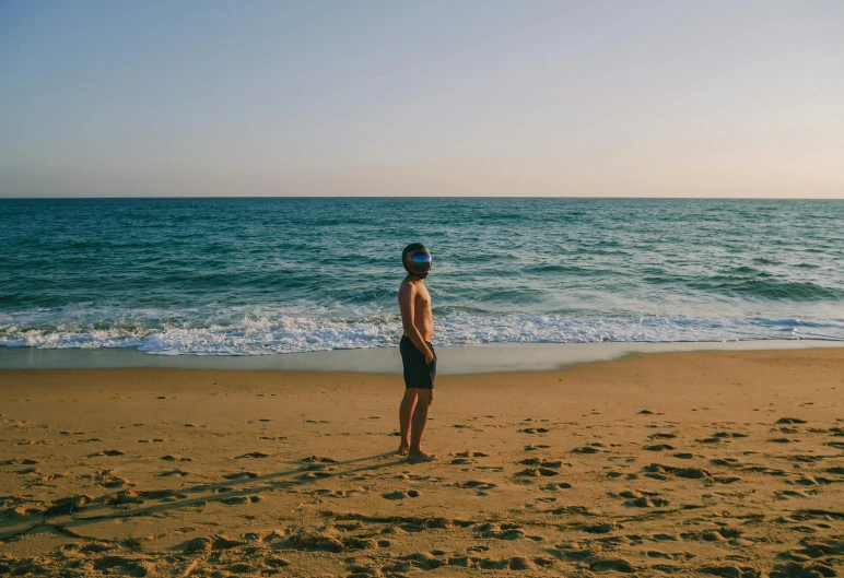 a man standing on top of a sandy beach next to the ocean, pexels contest winner, profile image, full body image, sunfaded, tiny person watching